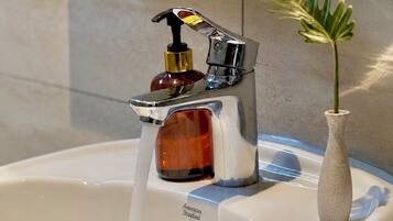 Un lavabo de salle de bain avec un robinet chromé, un distributeur de savon et un vase avec une plante.