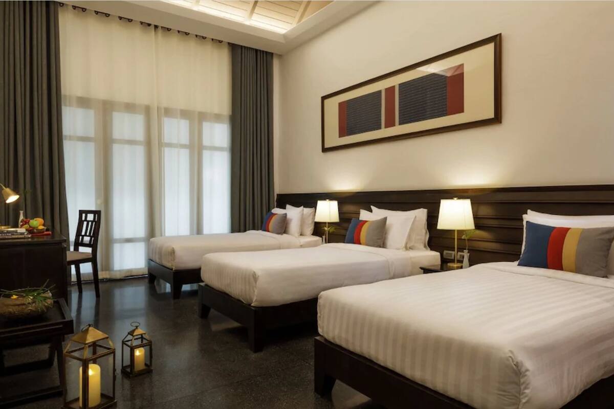 A hotel room with two beds, a desk with a lamp, a chair, and a large framed picture on the wall.