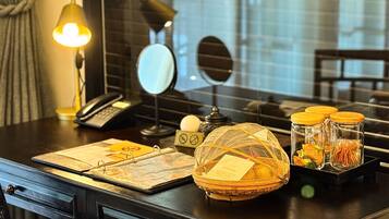 A hotel room desk with a lamp, phone, mirror, and decorative items including a basket and jars.