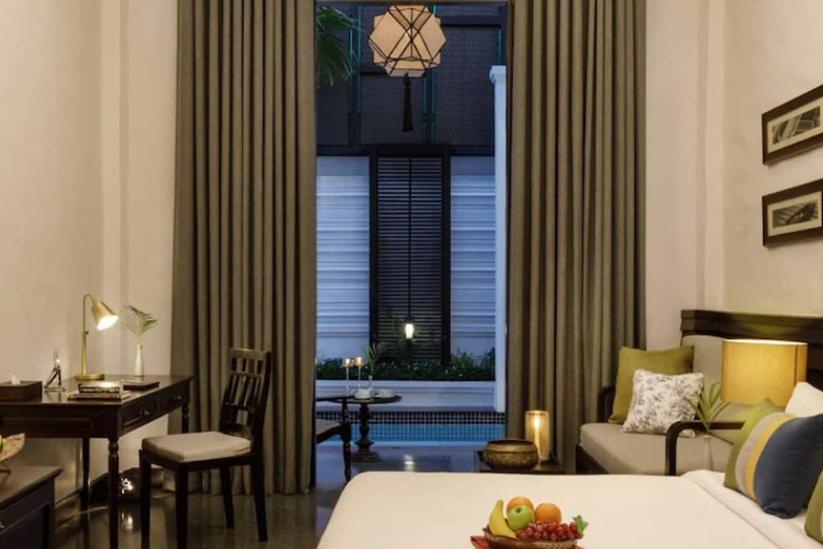 A hotel room with a bed, a desk, a chair, a sofa, and a view of a pool.