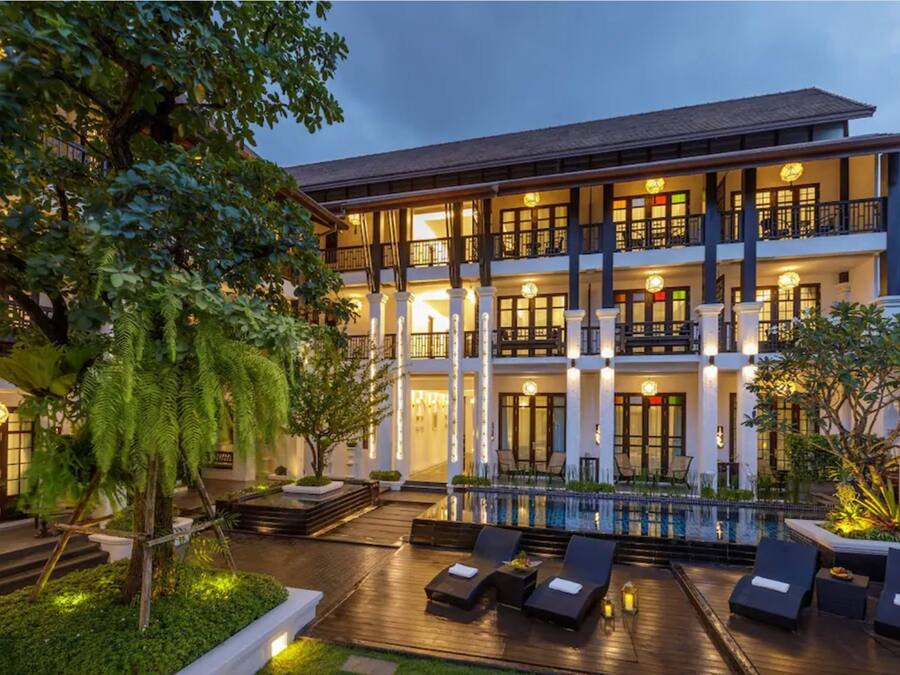 Un hotel de varios pisos con zona de piscina, asientos al aire libre y una fachada bien iluminada.