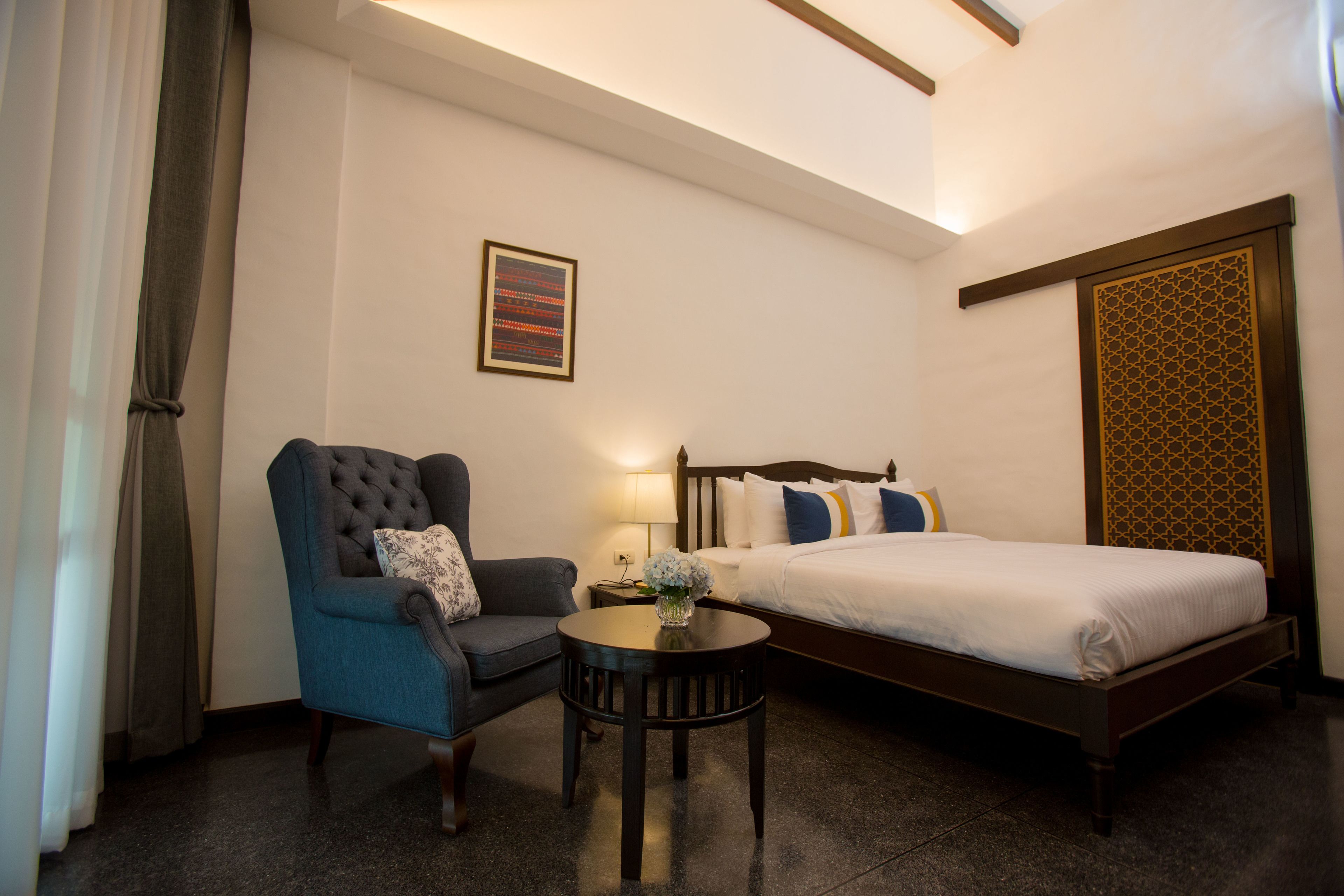 A hotel room with a bed, a chair, a small table, and a wall-mounted artwork.