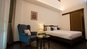 A hotel room with a bed, a chair, a small table, and a wall-mounted artwork.
