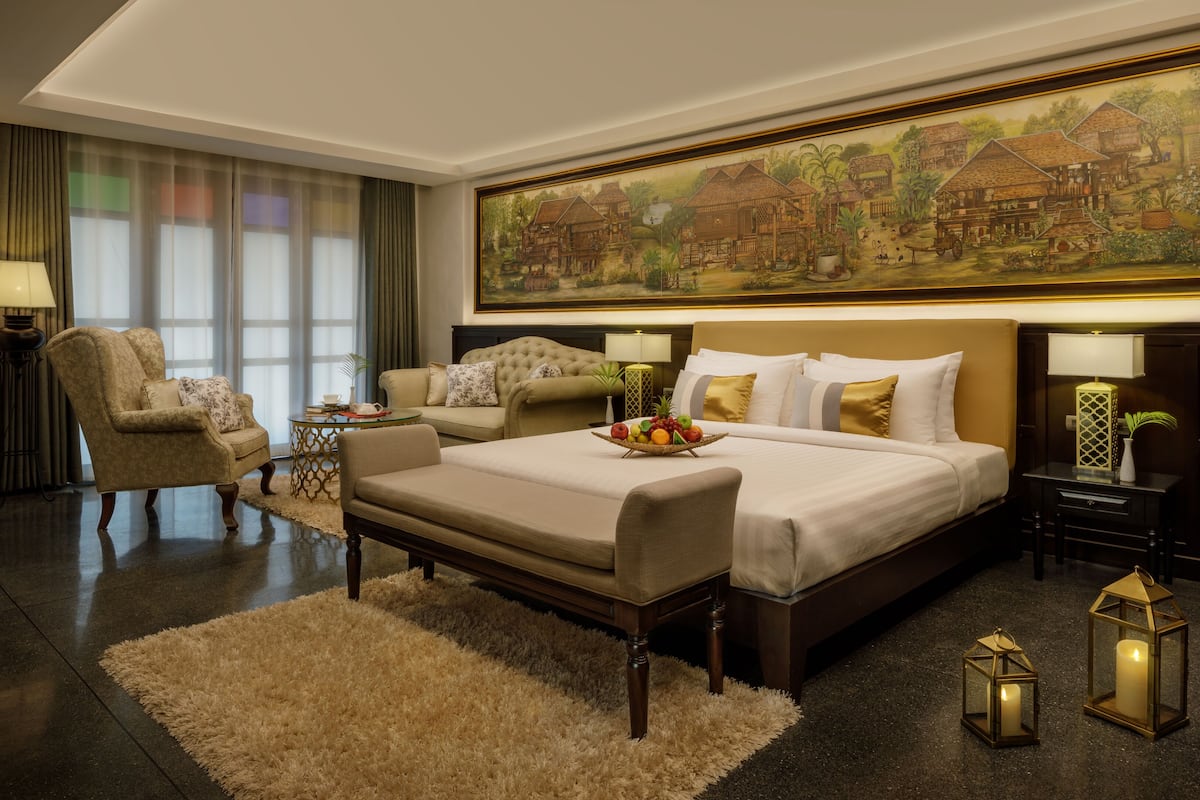 A hotel room with a large bed, a sofa, a chair, a small table, and a painting on the wall.
