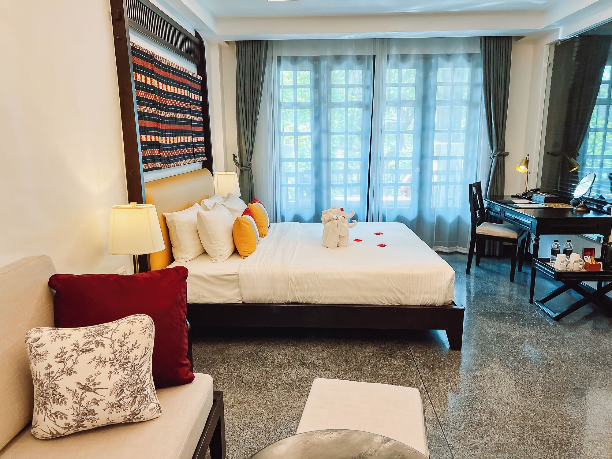 Une chambre d’hôtel avec un lit, un bureau, une chaise, un canapé et une grande fenêtre avec des rideaux.