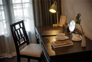 Un escritorio de madera con una silla, una lámpara, un espejo, una tetera, una taza, un platillo y libros.