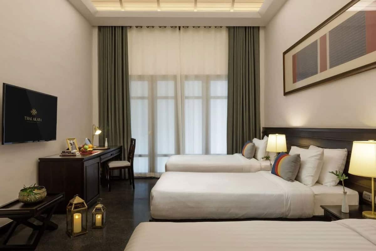 A hotel room with two beds, a desk with a TV, and a large window with curtains.