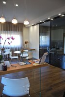 A modern office space with a glass partition, white chairs, a wooden reception desk, and hanging pendant lights.