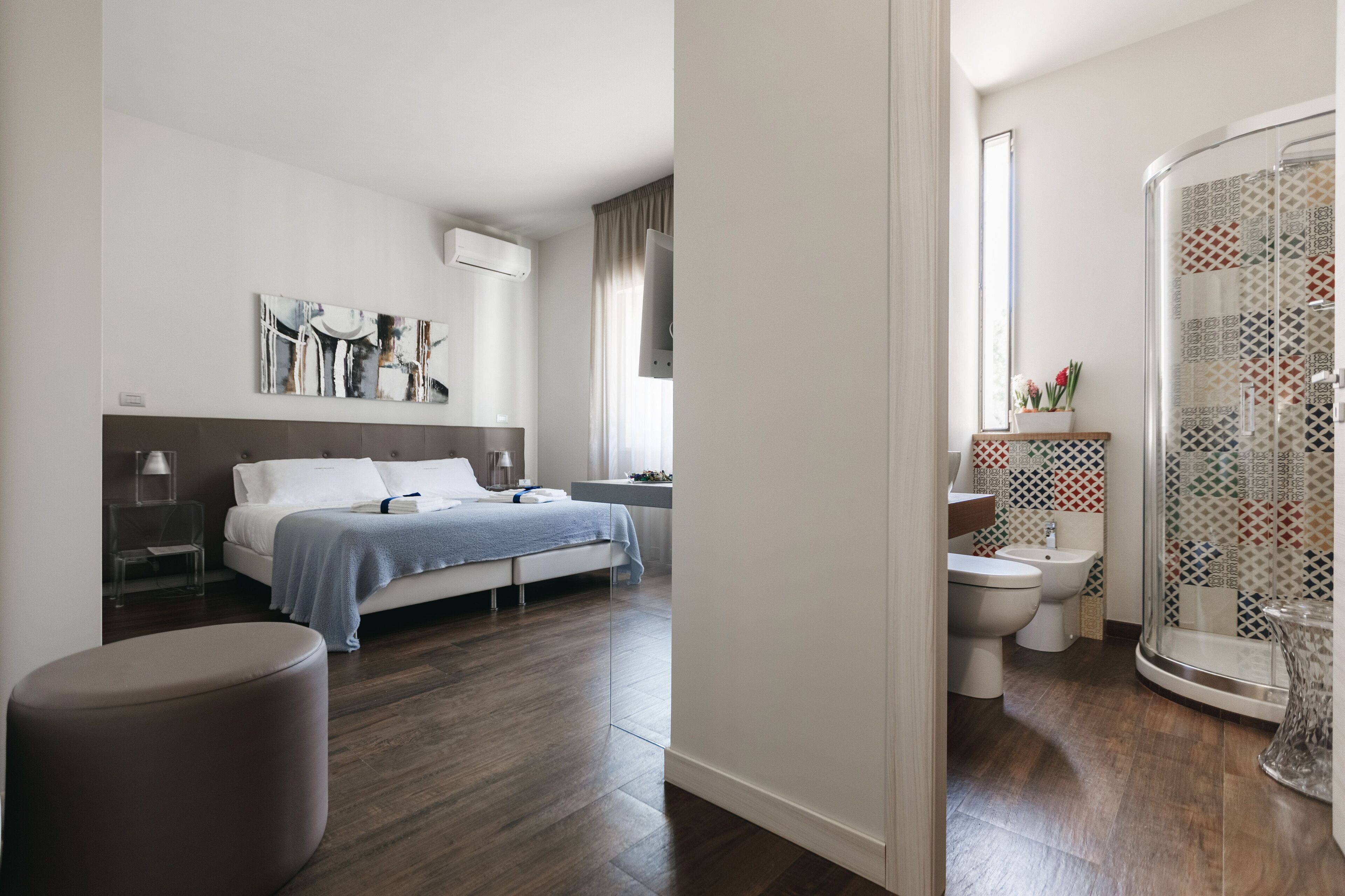 A modern bedroom with a bed, bedside table, and a large window. The bathroom includes a shower, toilet, and sink.
