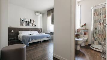 Un dormitorio moderno con cama, mesita de noche y un ventanal grande. El baño tiene ducha, inodoro y lavabo.