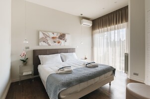 Un dormitorio moderno con una cama grande, una mesita de noche con lámpara, aire acondicionado instalado en la pared y una ventana con cortinas translúcidas.