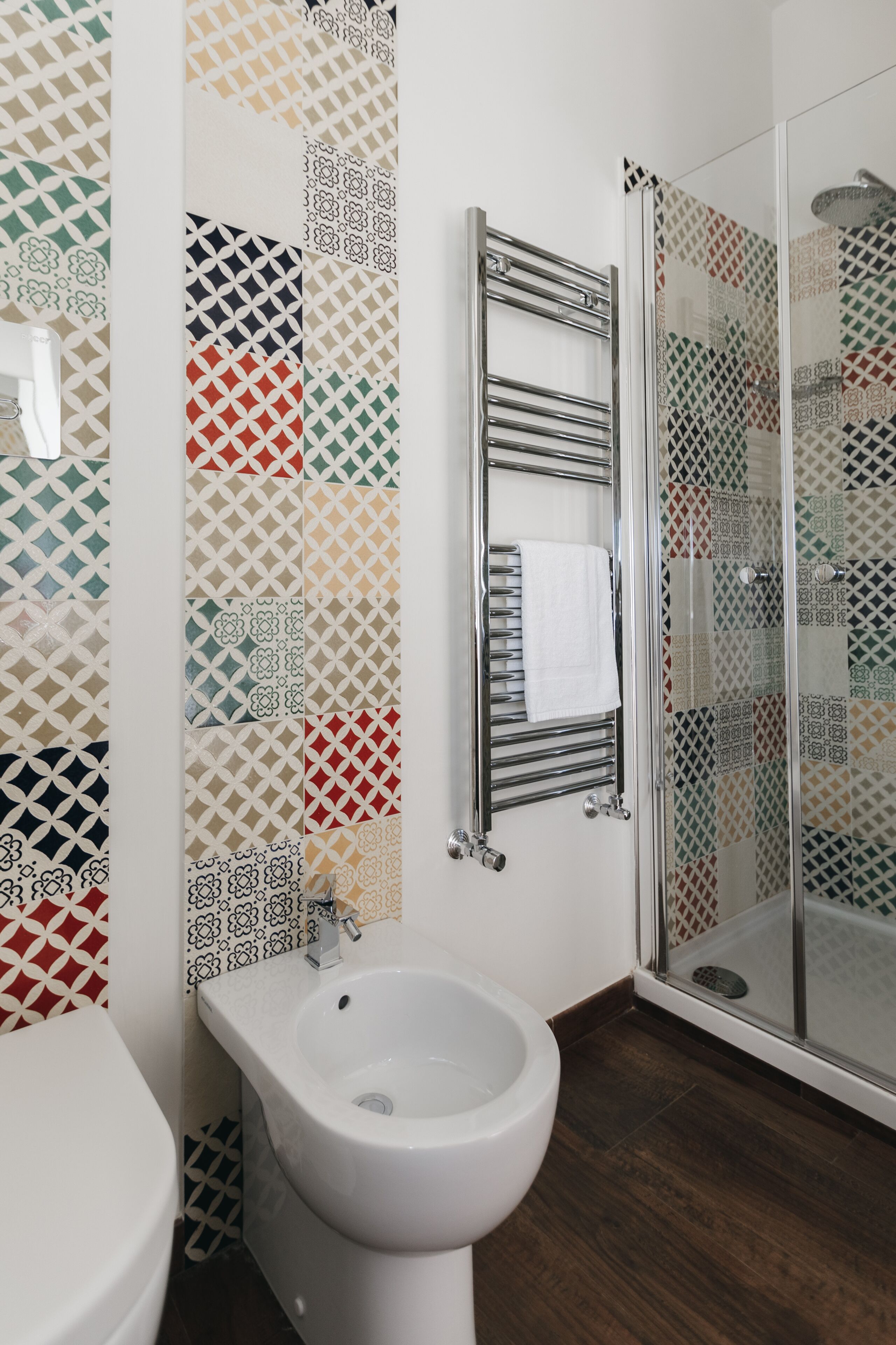 Un baño con bidé, cabina de ducha de vidrio y pared con diseño.