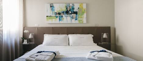 A hotel room with a large bed, two bedside tables, a wall-mounted abstract painting, and a window with curtains.