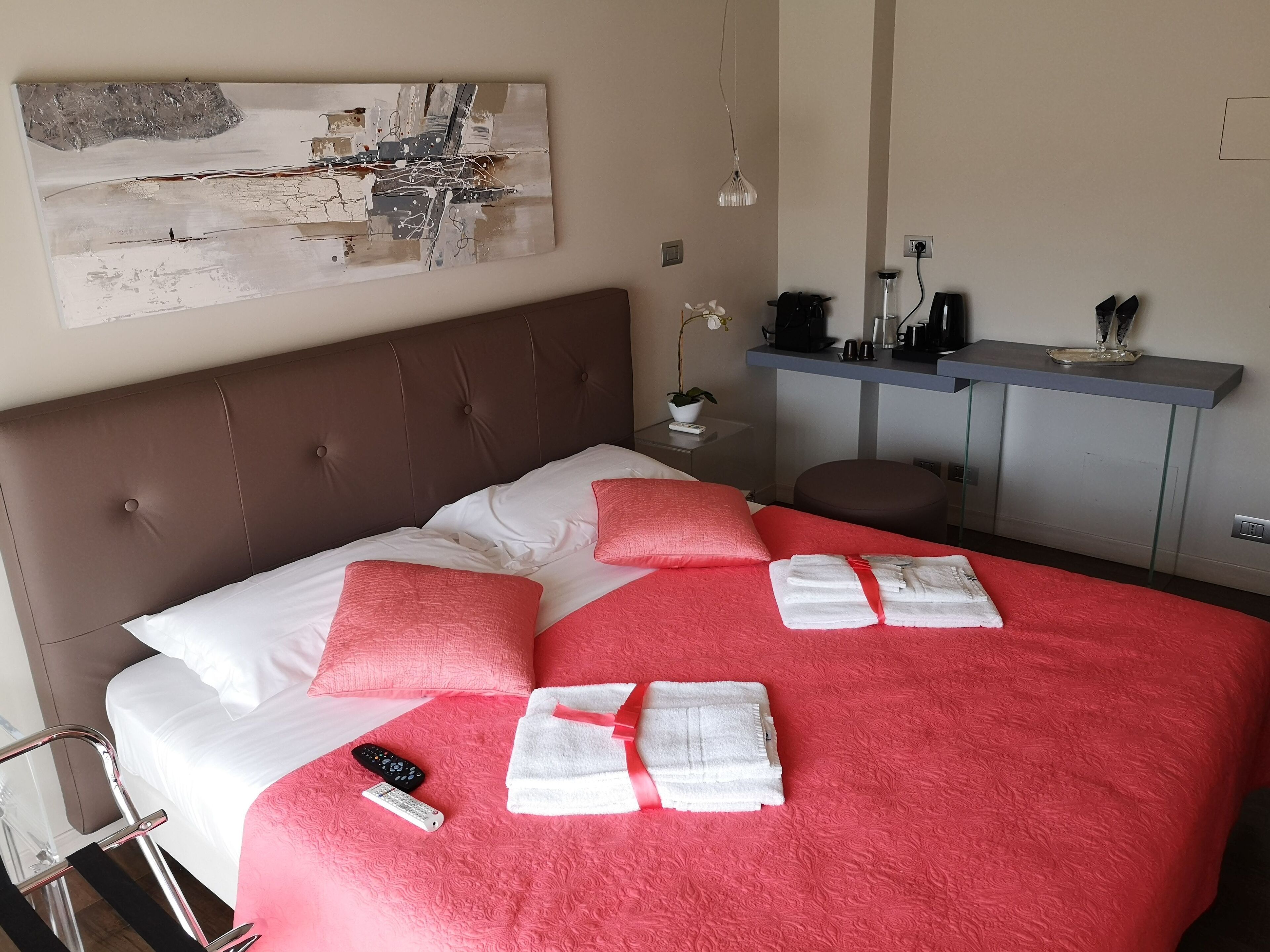 A hotel room with a large bed, red and white bedding, a remote control, and a towel on the bed.