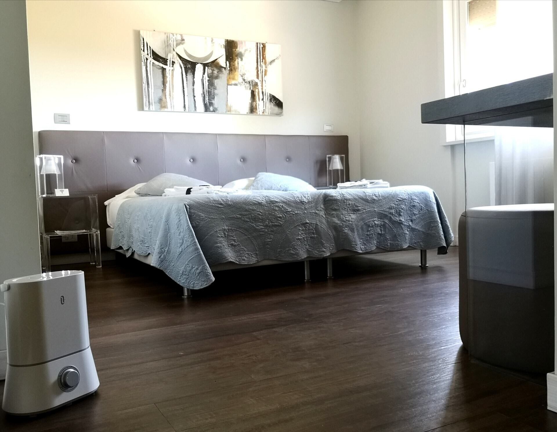 A modern hotel room with a large bed, a bedside table, a lamp, and a wall-mounted artwork.