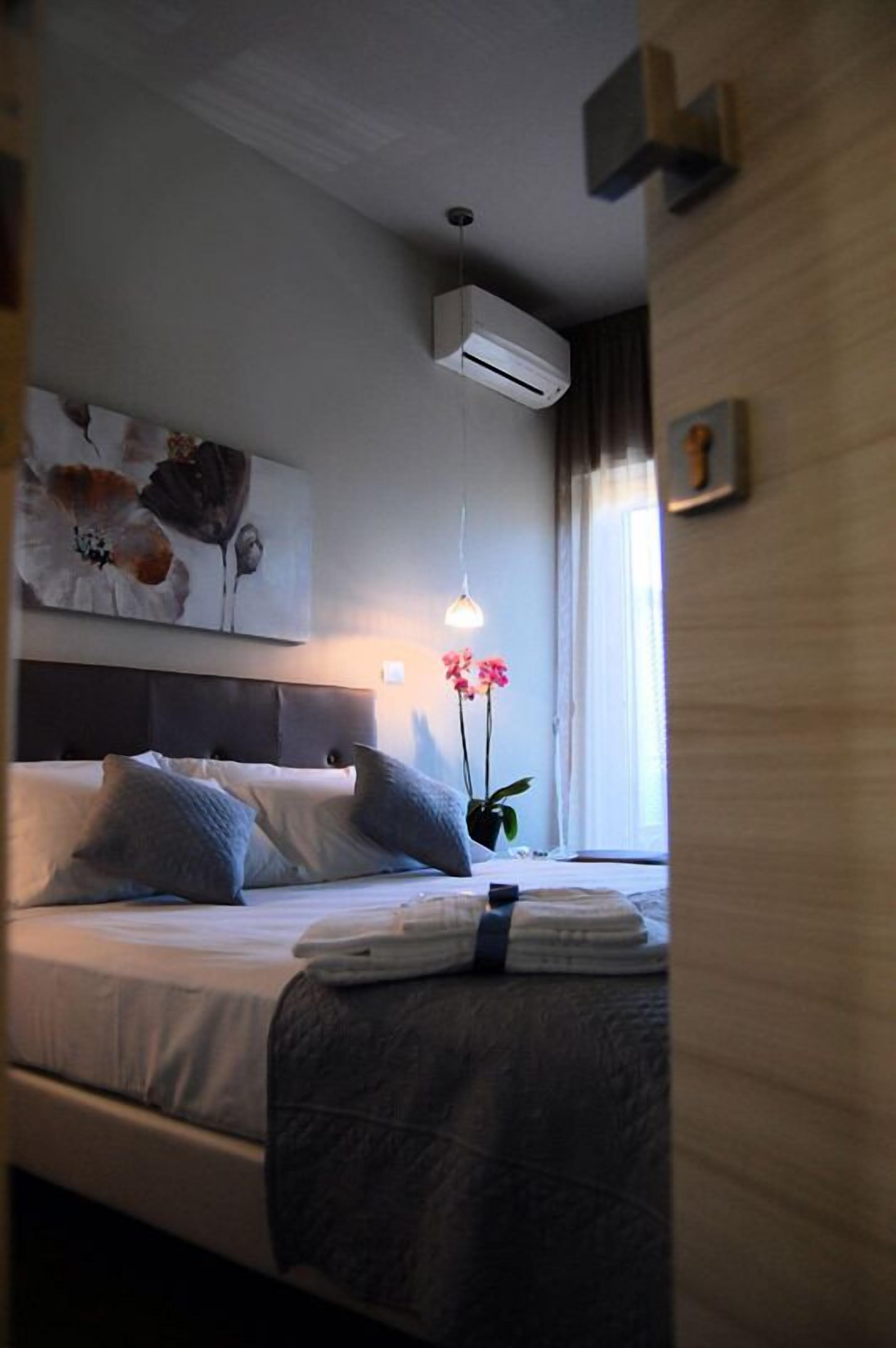 Una habitación de hotel con cama, aire acondicionado de pared, lámpara colgante y una planta en maceta.