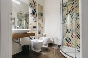 Un baño con un lavamanos blanco, dos inodoros y una cabina de ducha de vidrio.