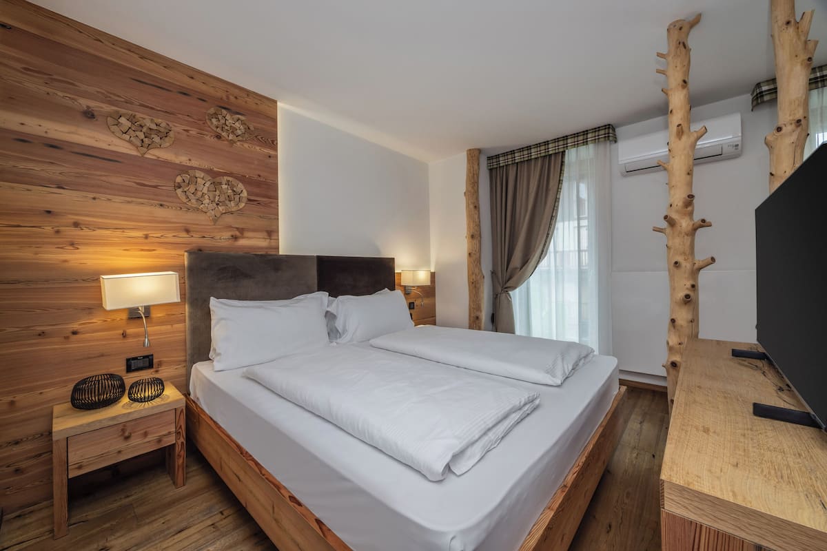 Un lit bien fait, avec du linge de lit blanc, une tête de lit en bois, une lampe de chevet et une petite table avec une lampe.