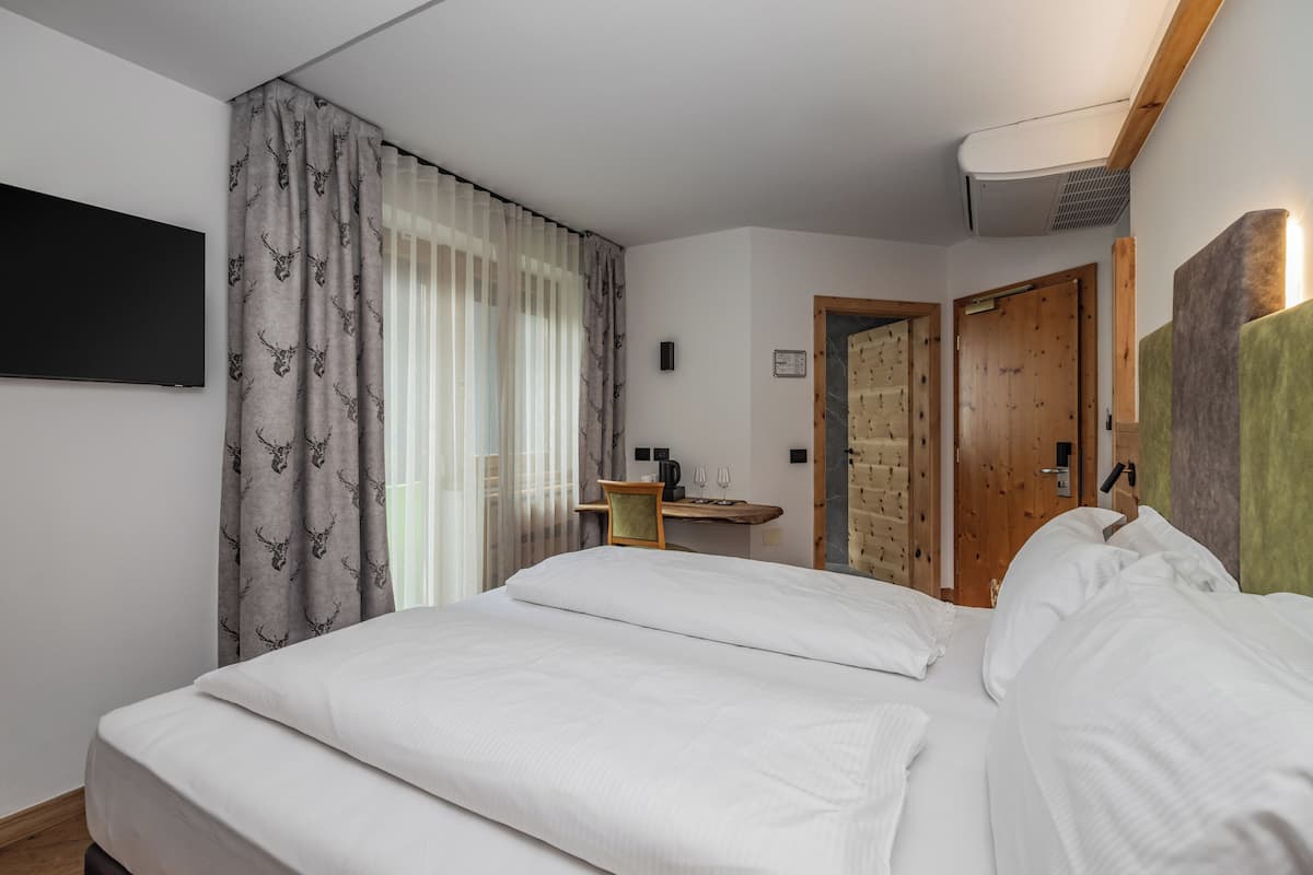 Une chambre avec un grand lit, un téléviseur à écran plat fixé au mur, une porte en bois et une petite table sur laquelle se trouvent une tasse et une soucoupe.