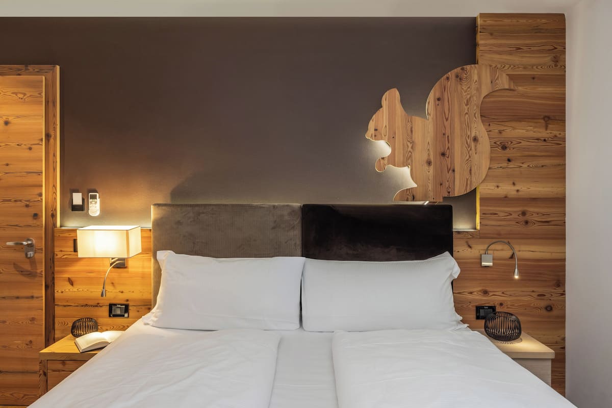 Un lit bien fait, avec du linge de lit blanc, une tête de lit en bois et un luminaire fixé au mur.