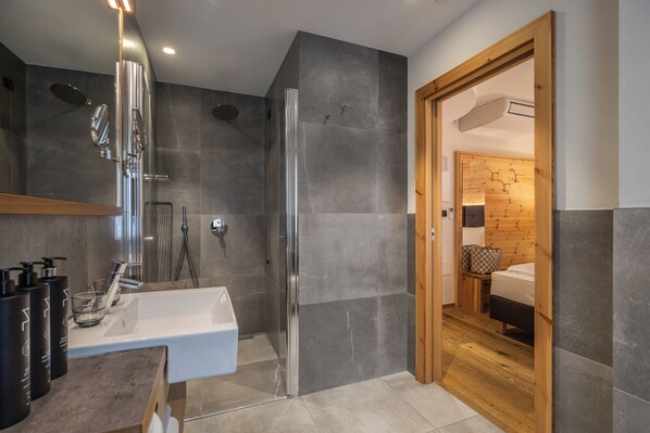 A modern bathroom with a glass-enclosed shower, a white sink, and a wooden door leading to a bedroom.