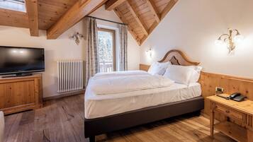 A bedroom with a wooden ceiling, a bed with white bedding, a bedside table with a phone, and a TV on a wooden cabinet.