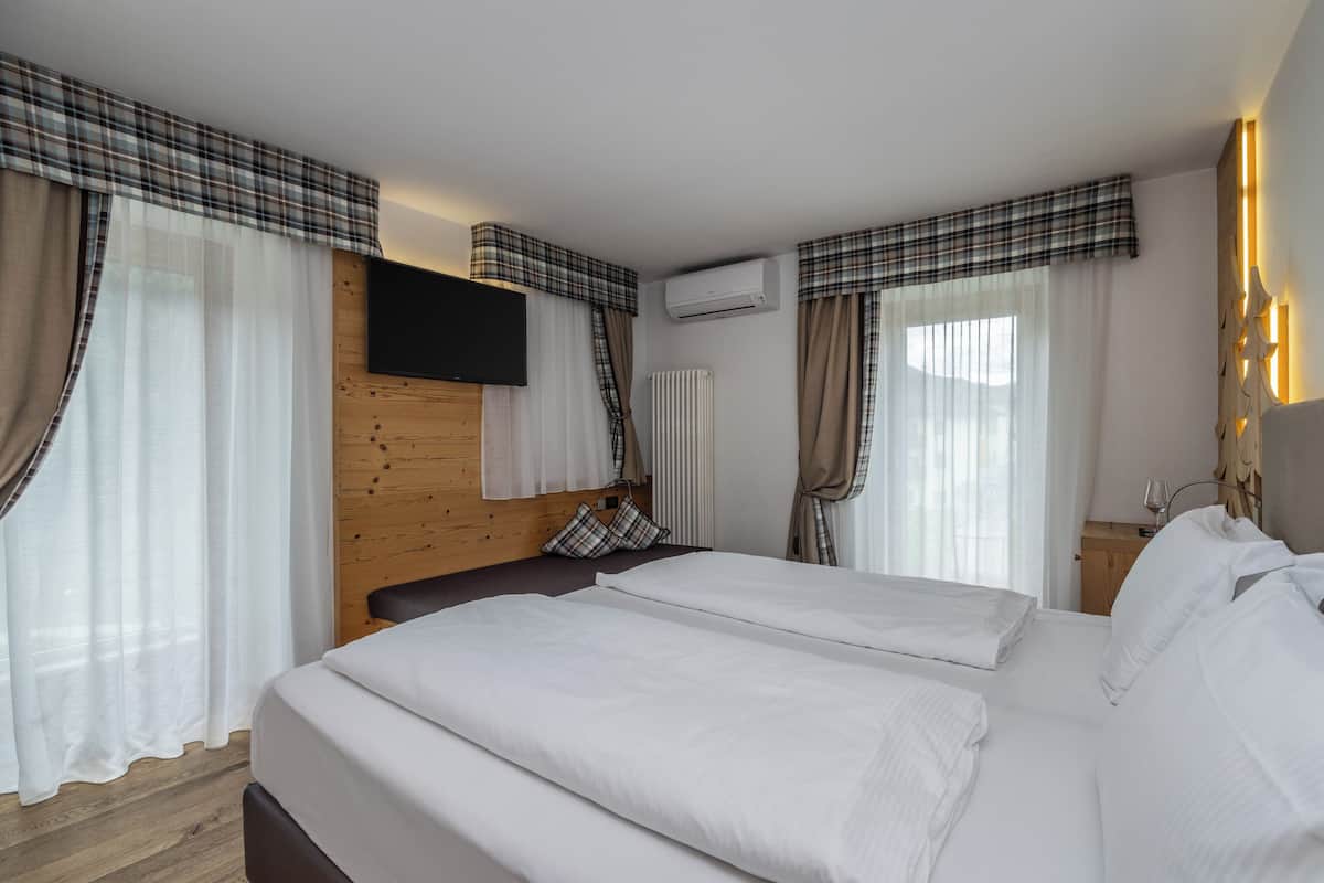 Une chambre d’hôtel avec deux lits, une tête de lit en bois, un téléviseur fixé au mur et une fenêtre avec des rideaux.