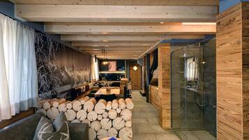 Un intérieur moderne avec un plafond en bois, un mur en pierre, une douche en verre et un coin salon agrémenté de bûches.