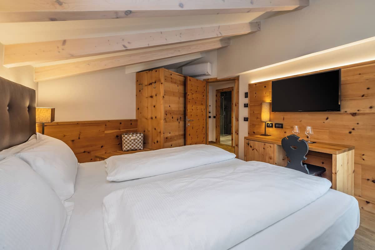 Une chambre avec un grand lit, une armoire en bois, un bureau avec un téléviseur à écran plat et une lampe.