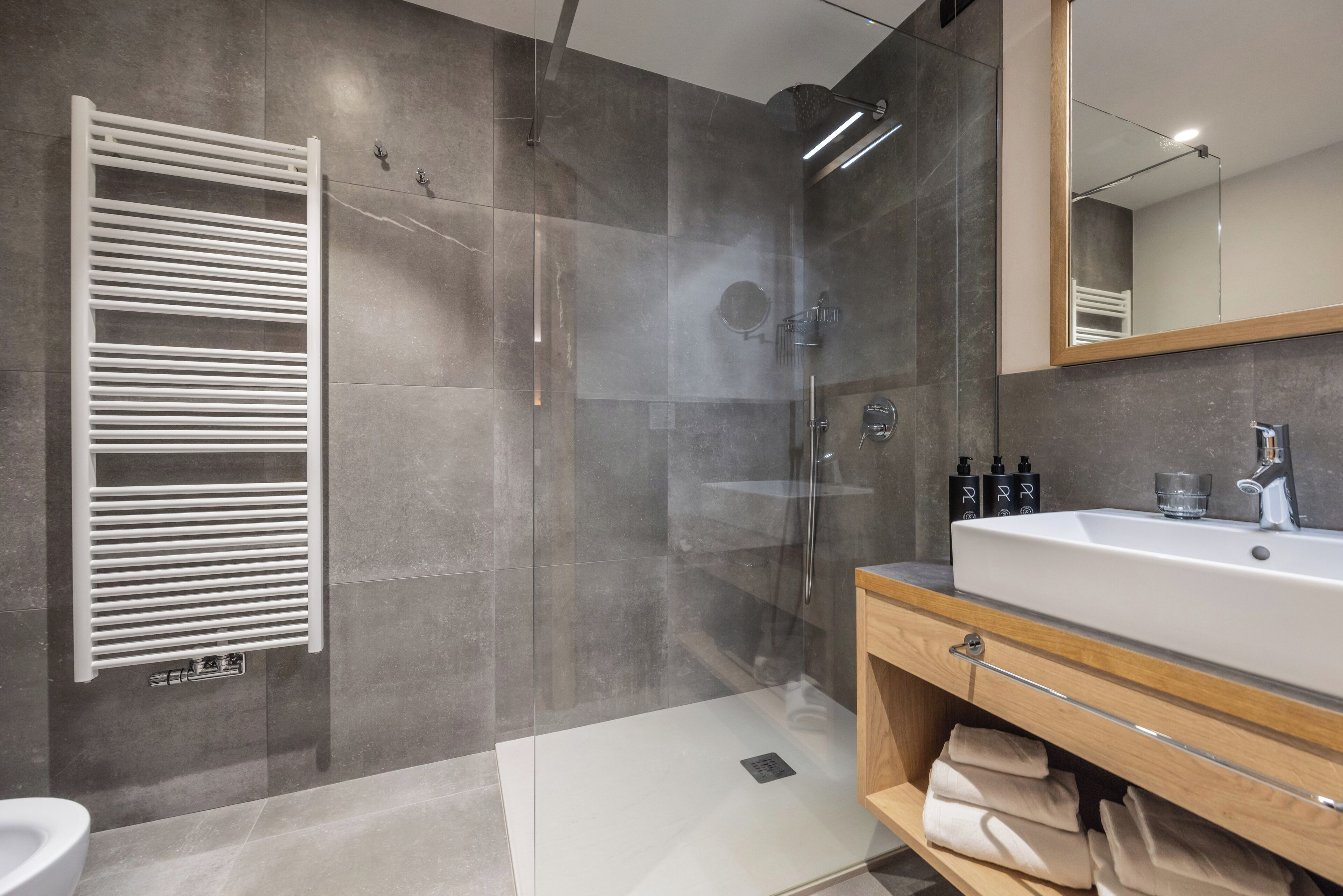 A modern bathroom with a glass-enclosed shower, a white sink, and a wooden vanity.