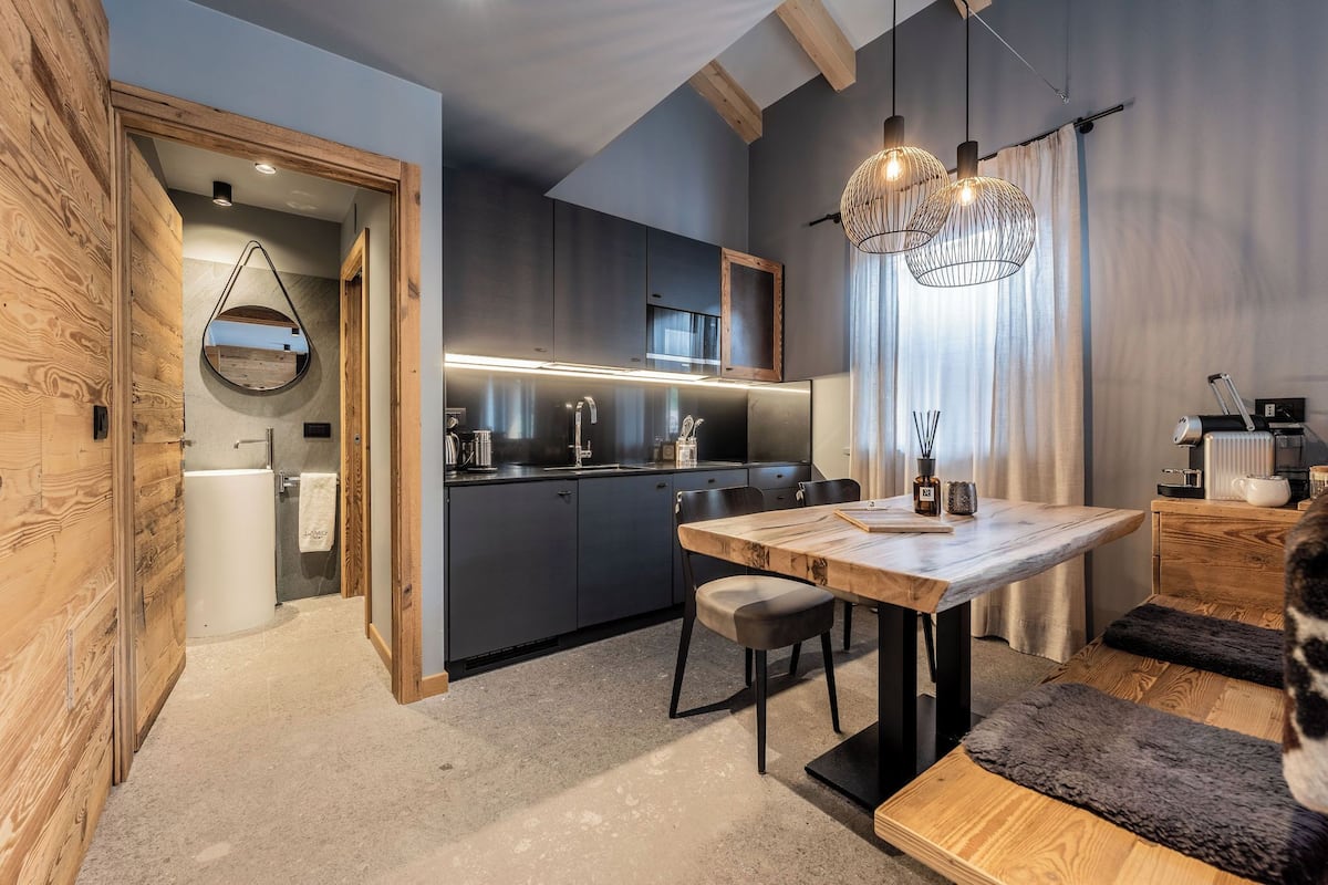 Une cuisine moderne avec des meubles de couleur sombre, une table à manger en bois et des luminaires suspendus.