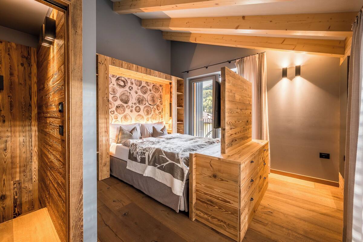 Une chambre à coucher avec une tête de lit en bois, un lit recouvert d’une couvre-lit à motifs, une commode en bois et une table de chevet.