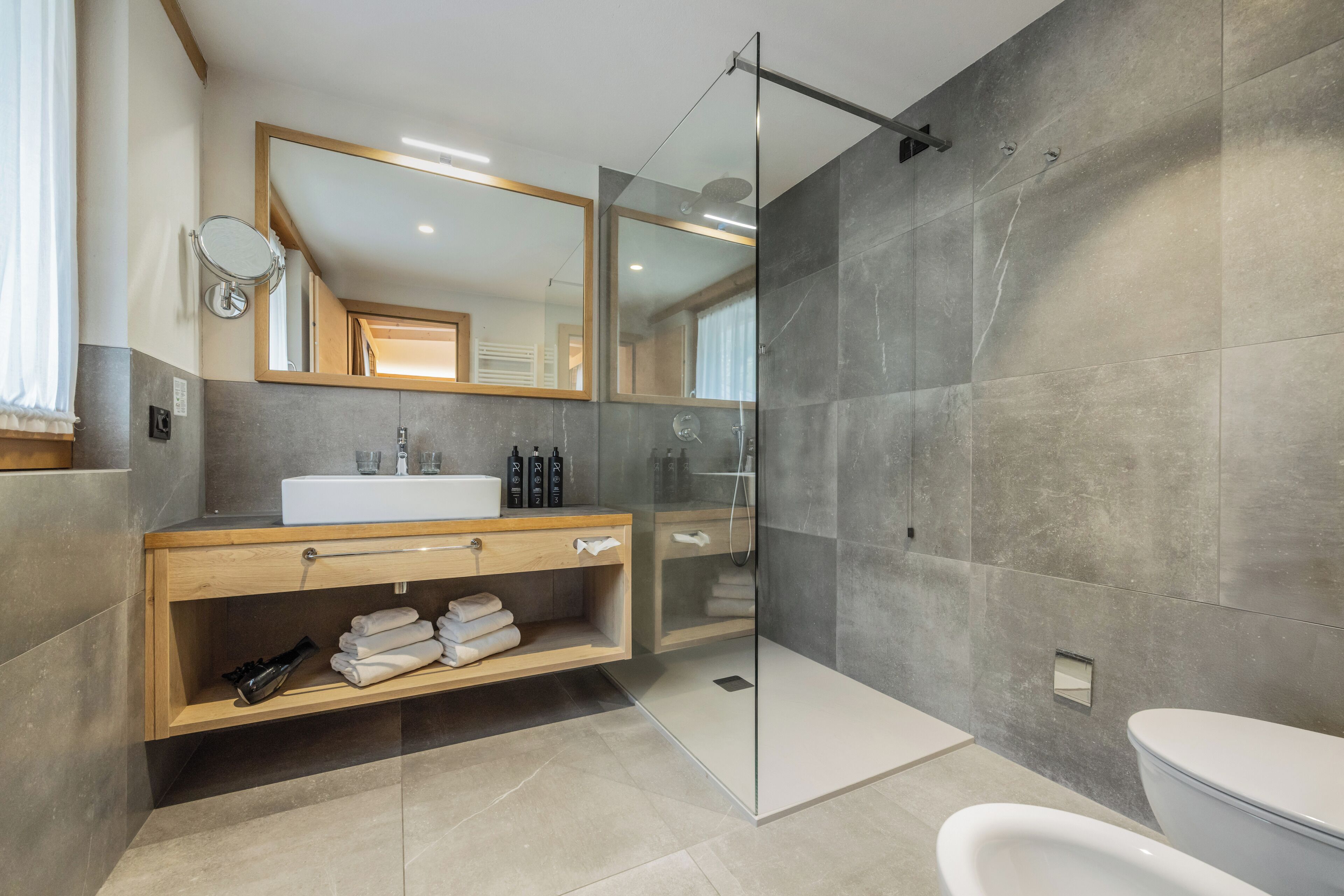 A modern bathroom with a glass-enclosed shower, a wooden vanity with a sink, and a large mirror.
