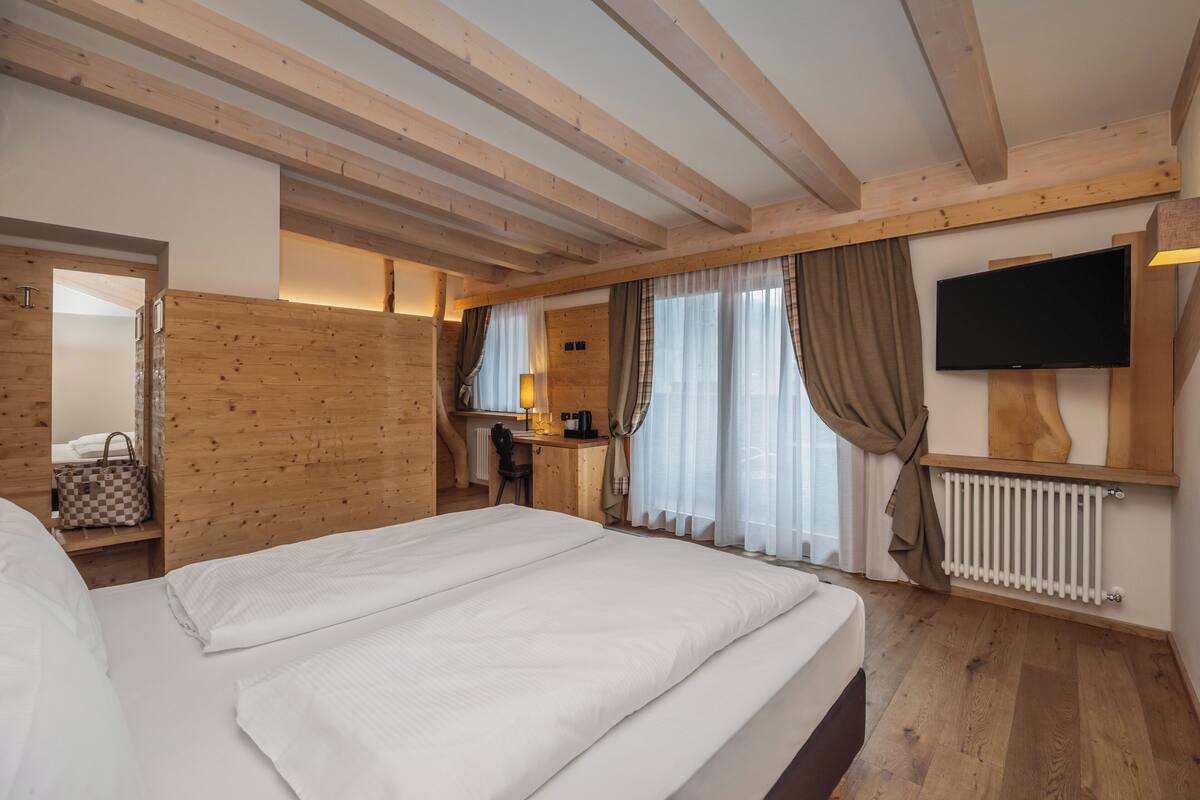 Une chambre d’hôtel avec un grand lit, des poutres apparentes en bois au plafond, un bureau avec une chaise, une télévision et un radiateur.
