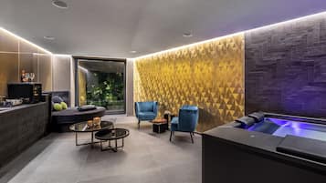 Ein moderner Wellnessbereich mit Massageliege, blauen Sesseln und einem kleinen Tisch mit Kerzen.