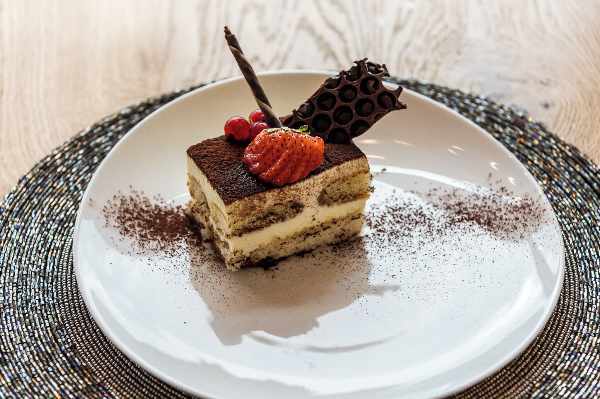 Una fetta di dolce stratificato su un piatto bianco, con un pezzo di cioccolato decorativo e una fragola sopra.