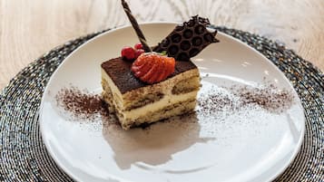 Una fetta di dolce stratificato su un piatto bianco, con un pezzo di cioccolato decorativo e una fragola sopra.