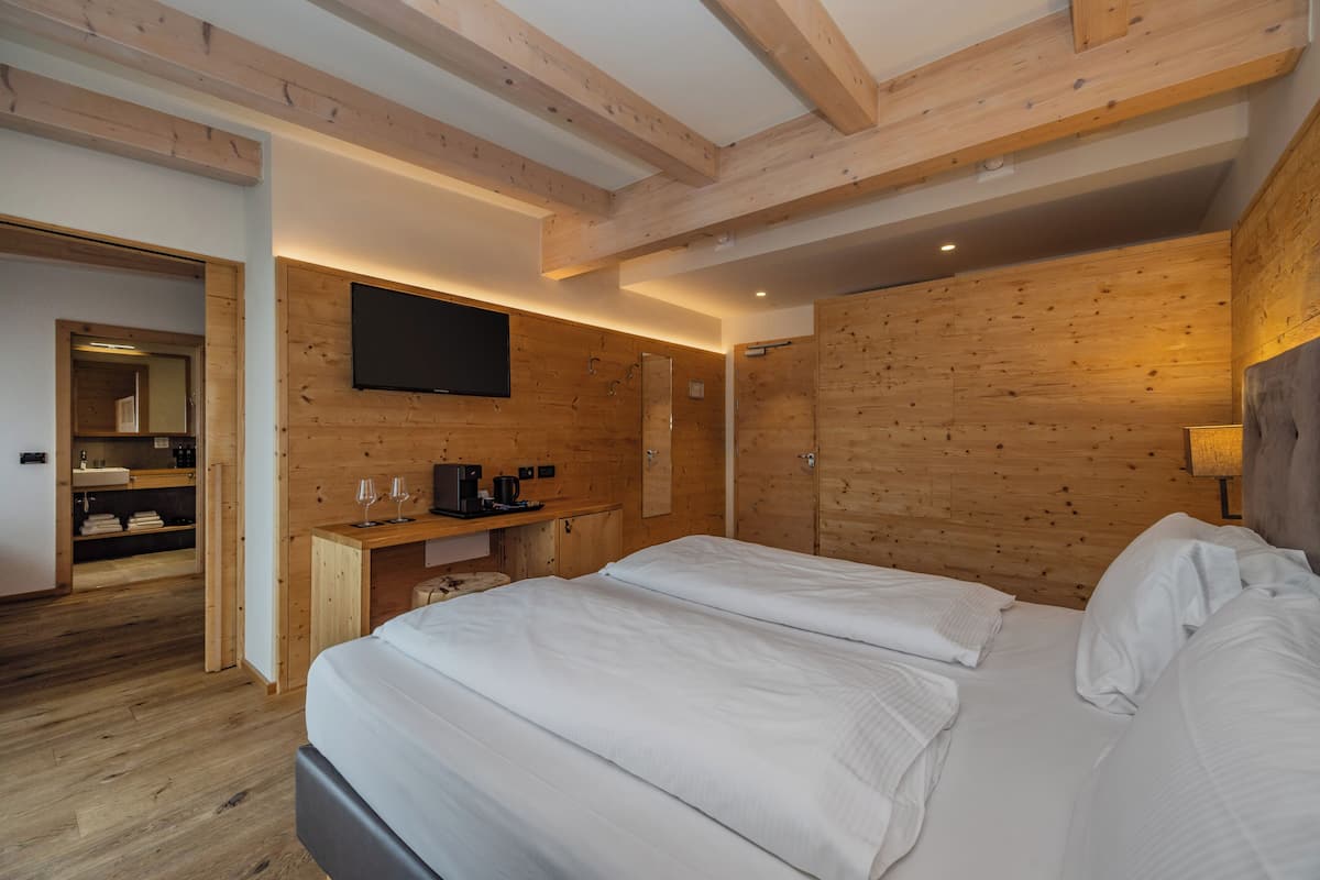 Une chambre d’hôtel moderne avec un plafond en bois, un téléviseur à écran plat fixé au mur, un lit avec du linge de maison blanc et un petit bureau équipé d’une machine à café.