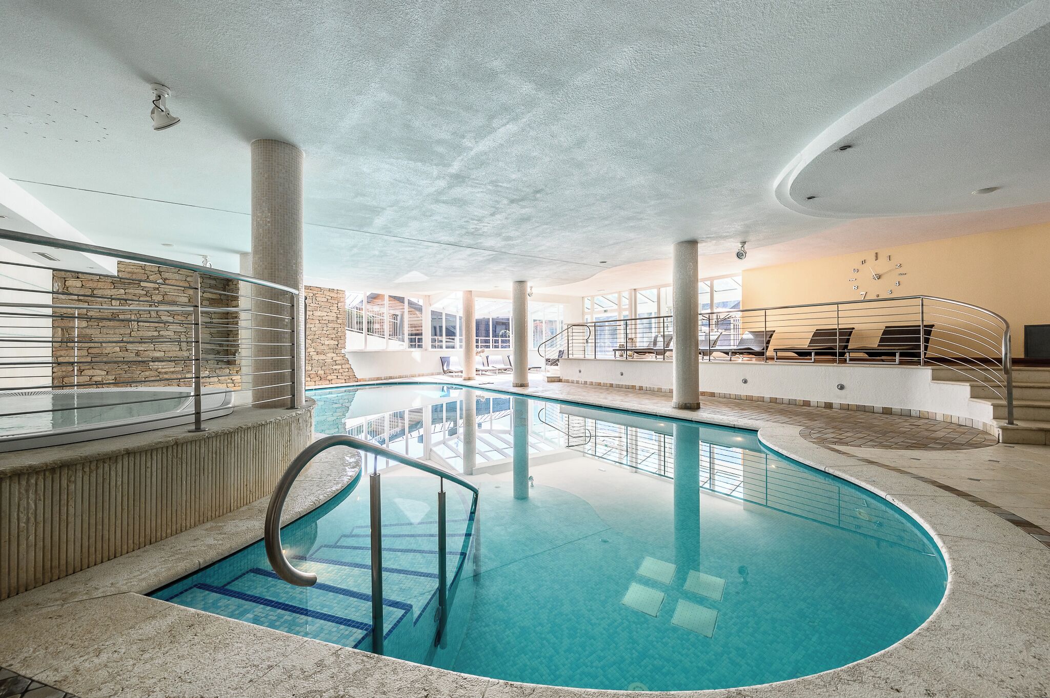 An indoor swimming pool with clear water, surrounded by stone walls and a glass railing.