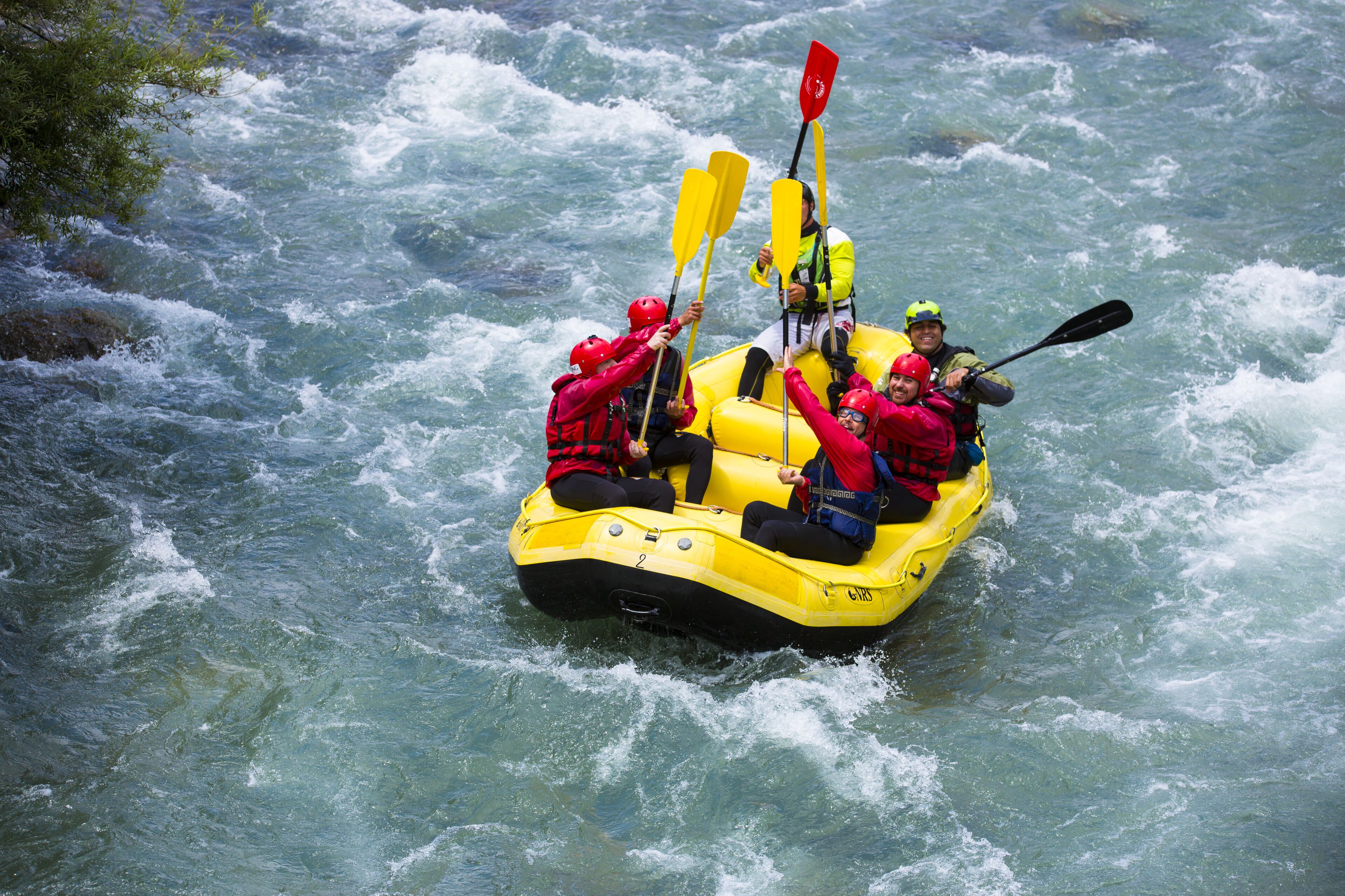 A group of people in a yellow raft navigating through a river with rapids.