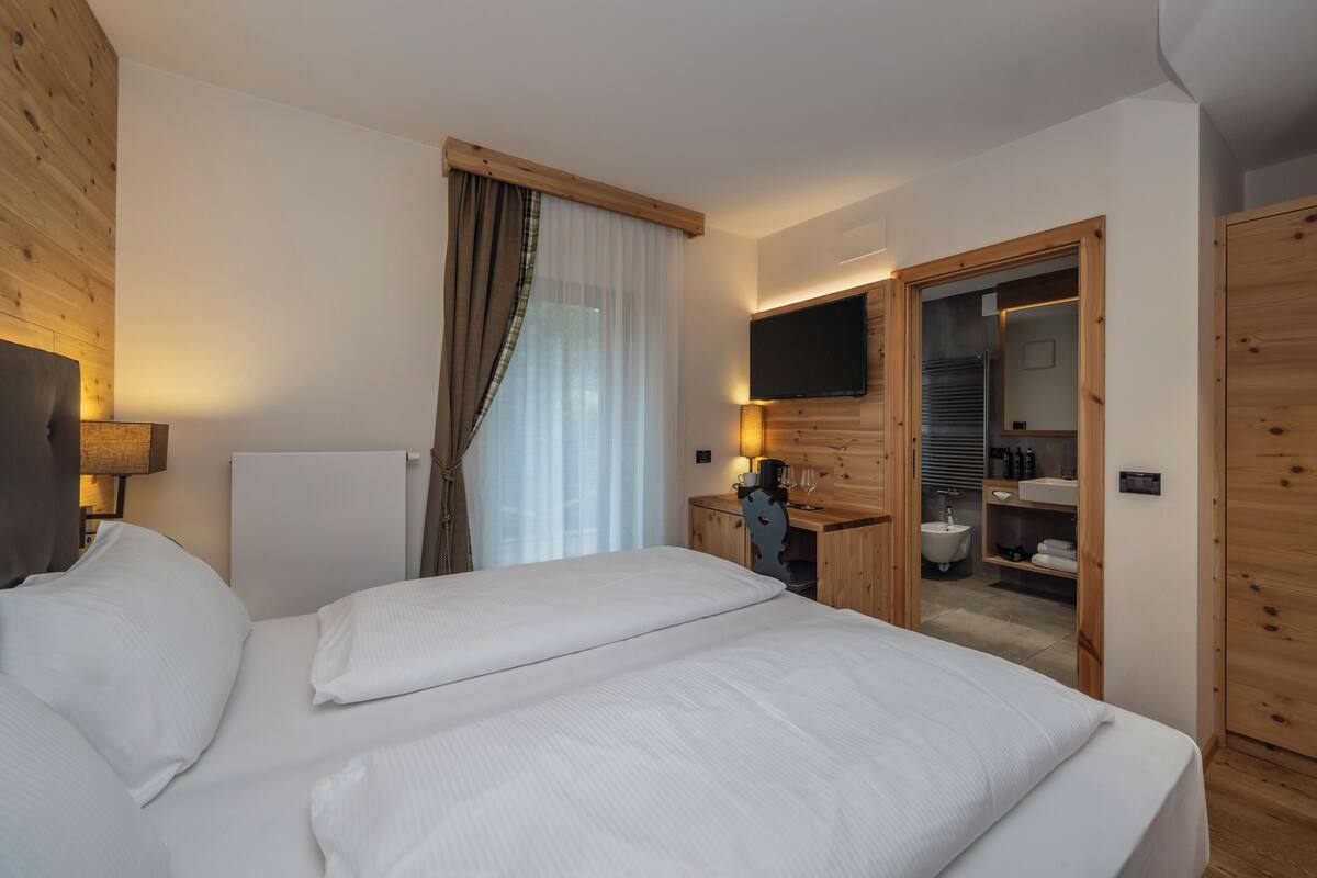 Une chambre d’hôtel avec un grand lit, un téléviseur fixé au mur, une armoire en bois et une salle de bain visible à travers une porte ouverte.