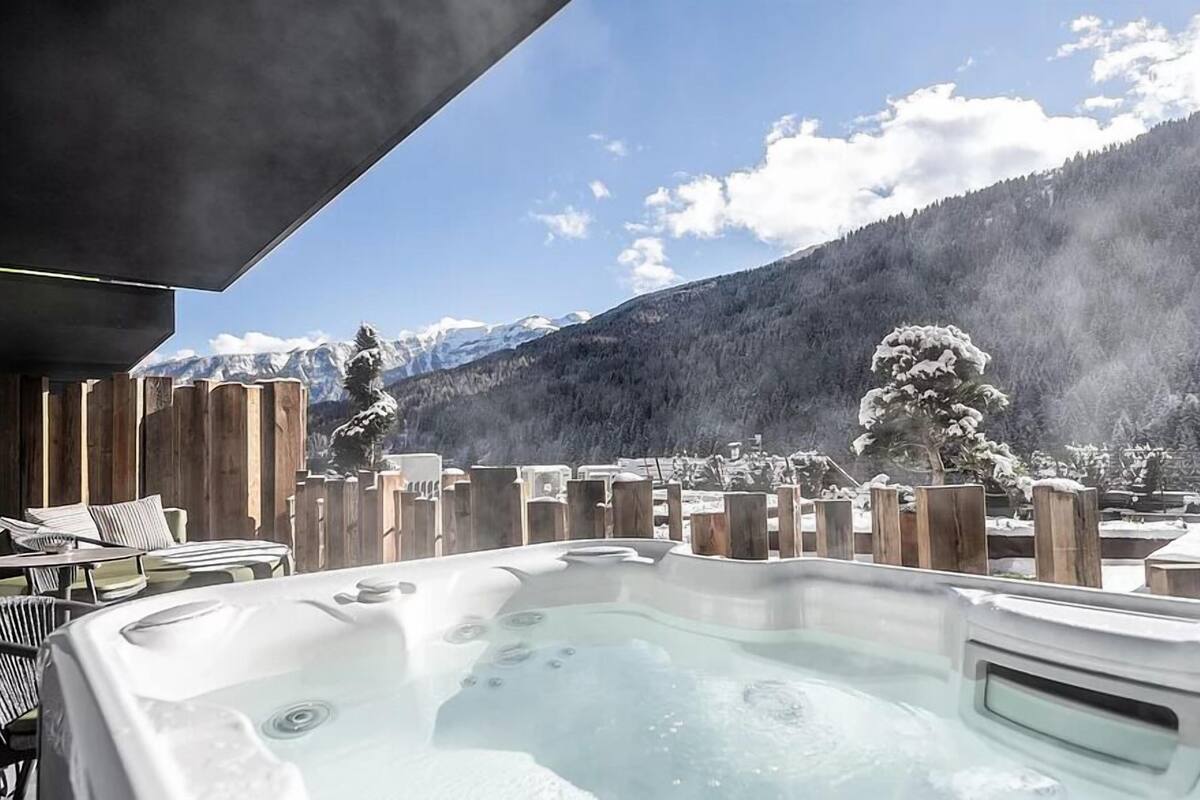 Un bain à remous avec vue sur les montagnes, une terrasse en bois et des chaises longues.