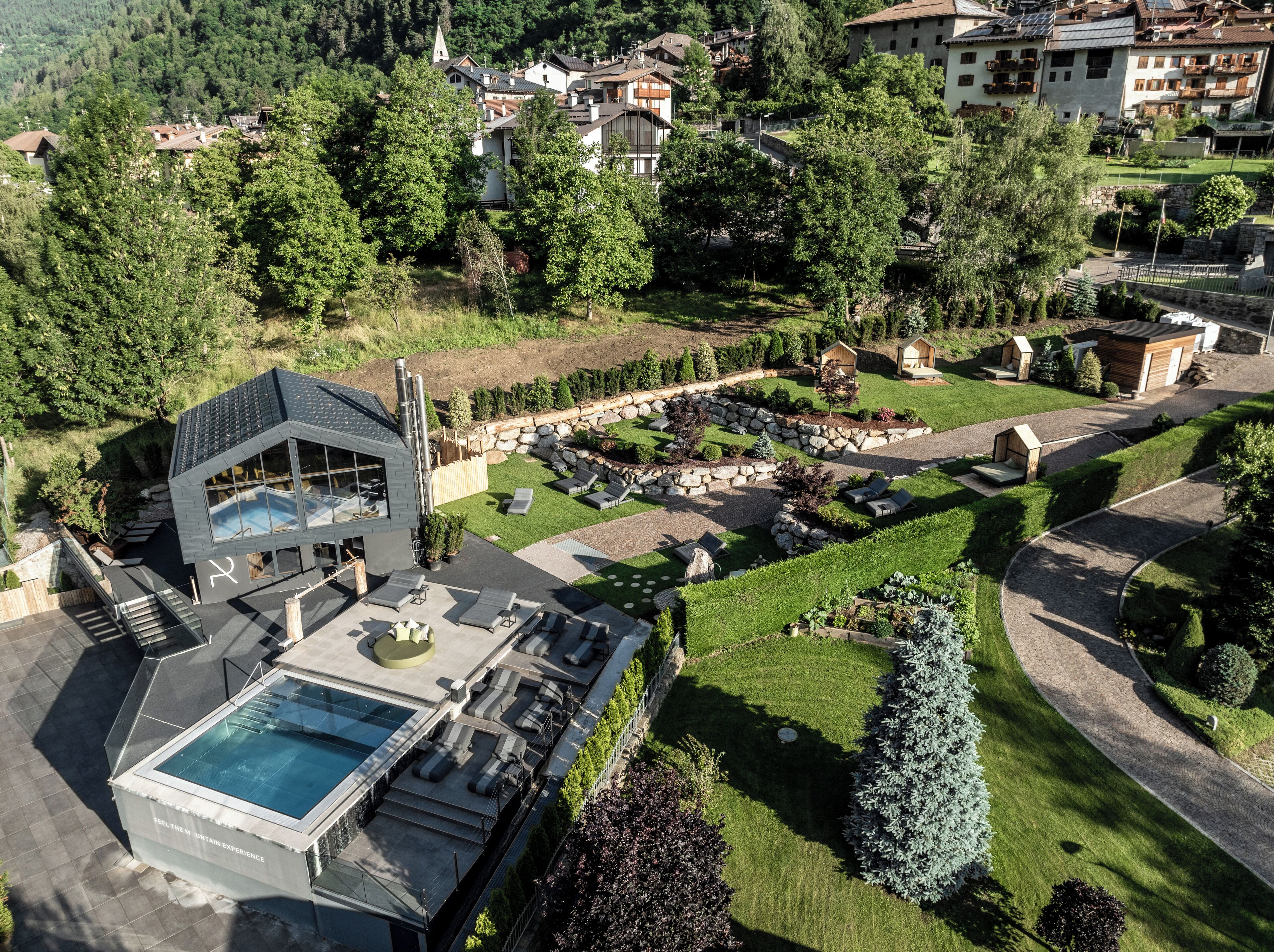 Un edificio moderno con piscina en la azotea y zona de estar al aire libre, rodeado de jardines cuidados y un muro de piedra.