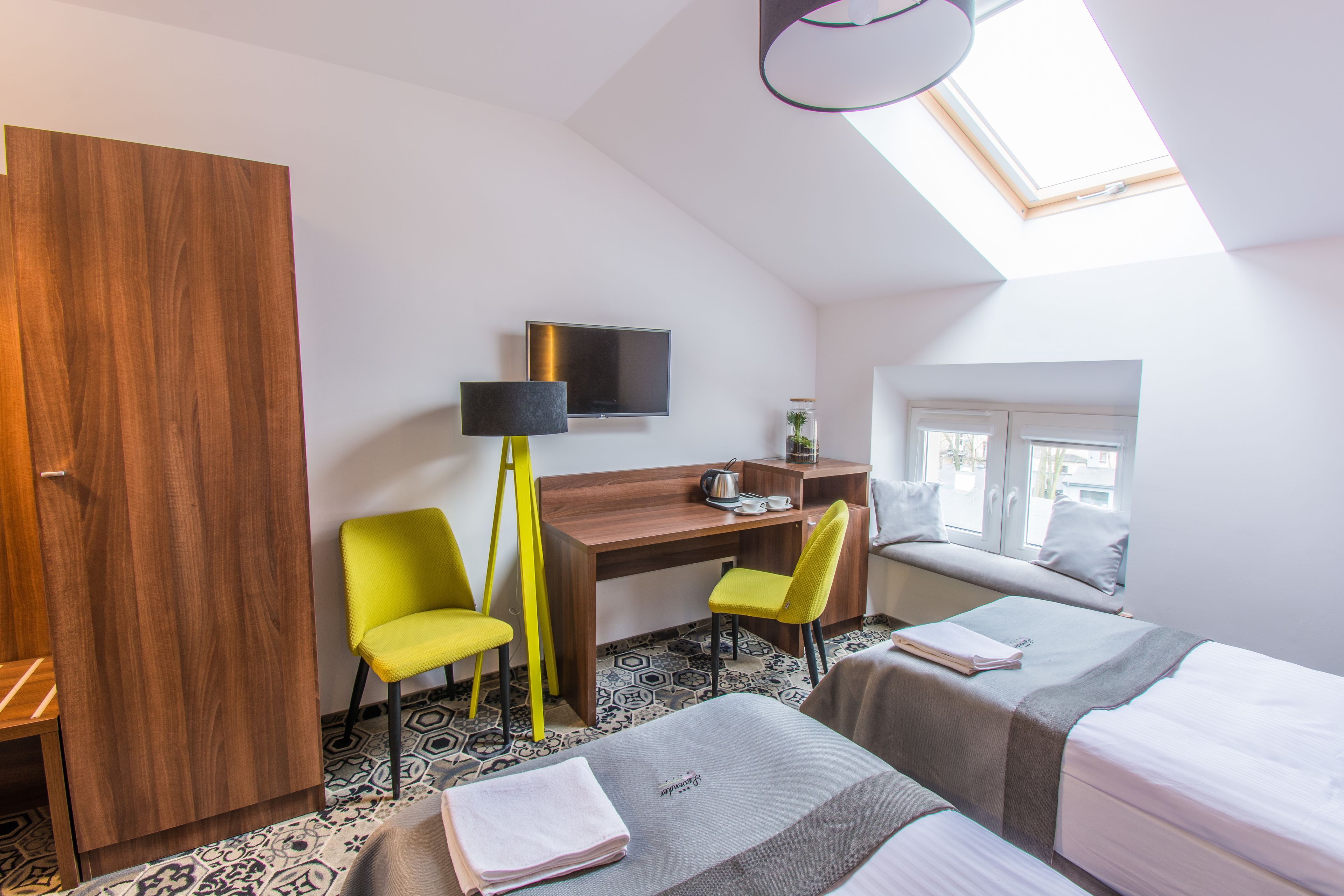Ein Hotelzimmer mit einem Holzkoffer, einem Schreibtisch mit Stuhl, einem Bett und einem Fenster mit Blick.