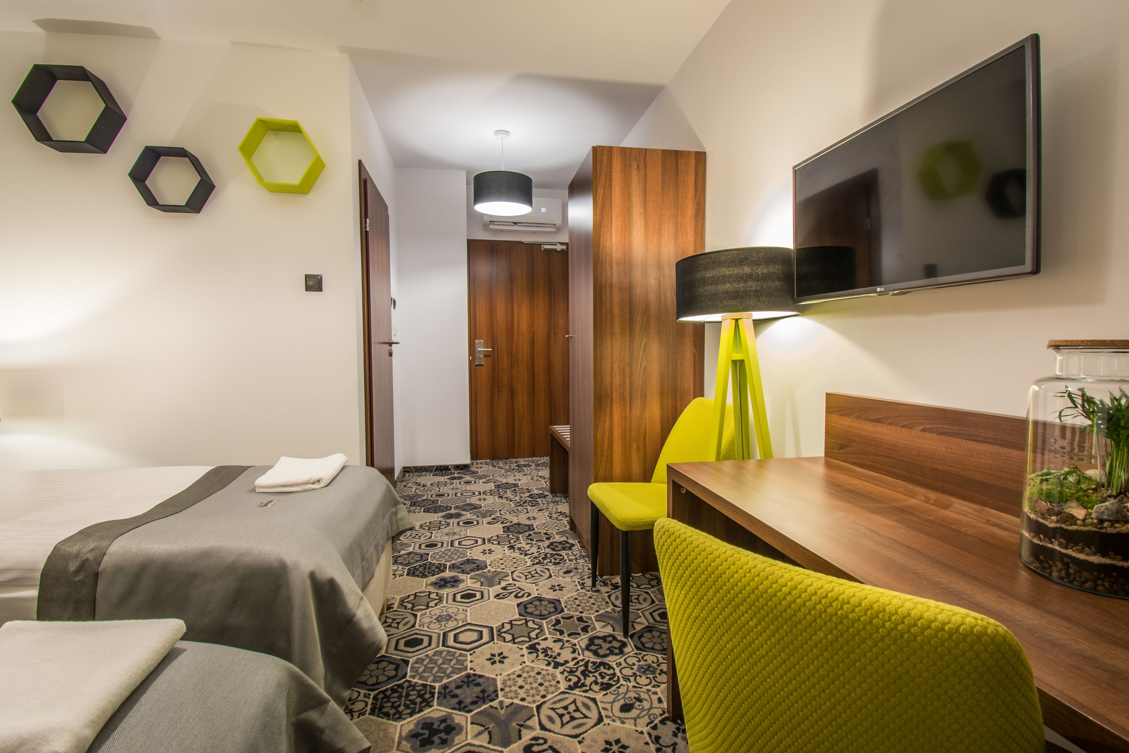 Habitación de hotel con dos camas, un escritorio de madera, una silla amarilla, un televisor y una lámpara fijada a la pared.
