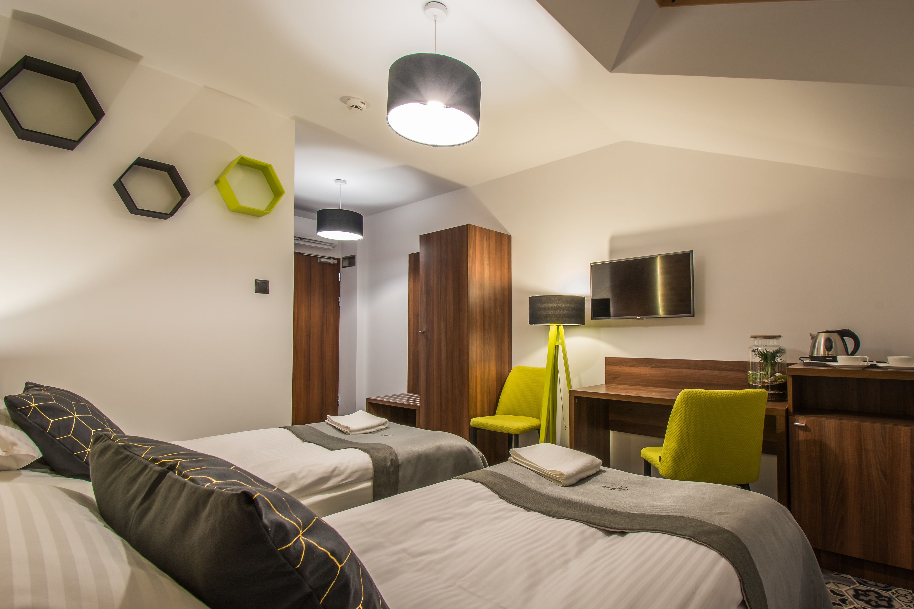 A hotel room with two beds, a desk, a chair, a TV, and a lamp.