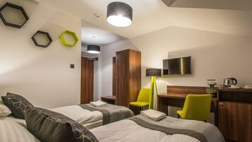 A hotel room with two beds, a desk, a chair, a TV, and a lamp.