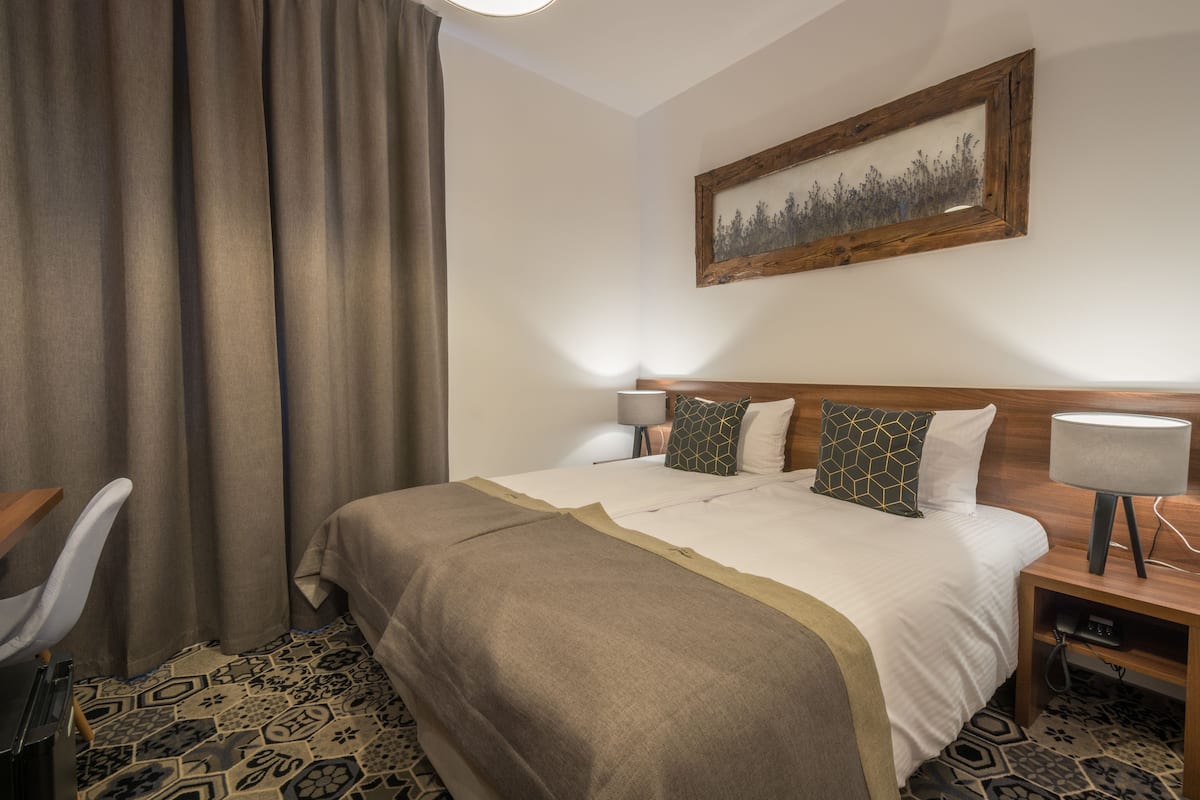 Una habitación de hotel con una cama grande, un escritorio, una silla y una mesita de noche con lámpara.