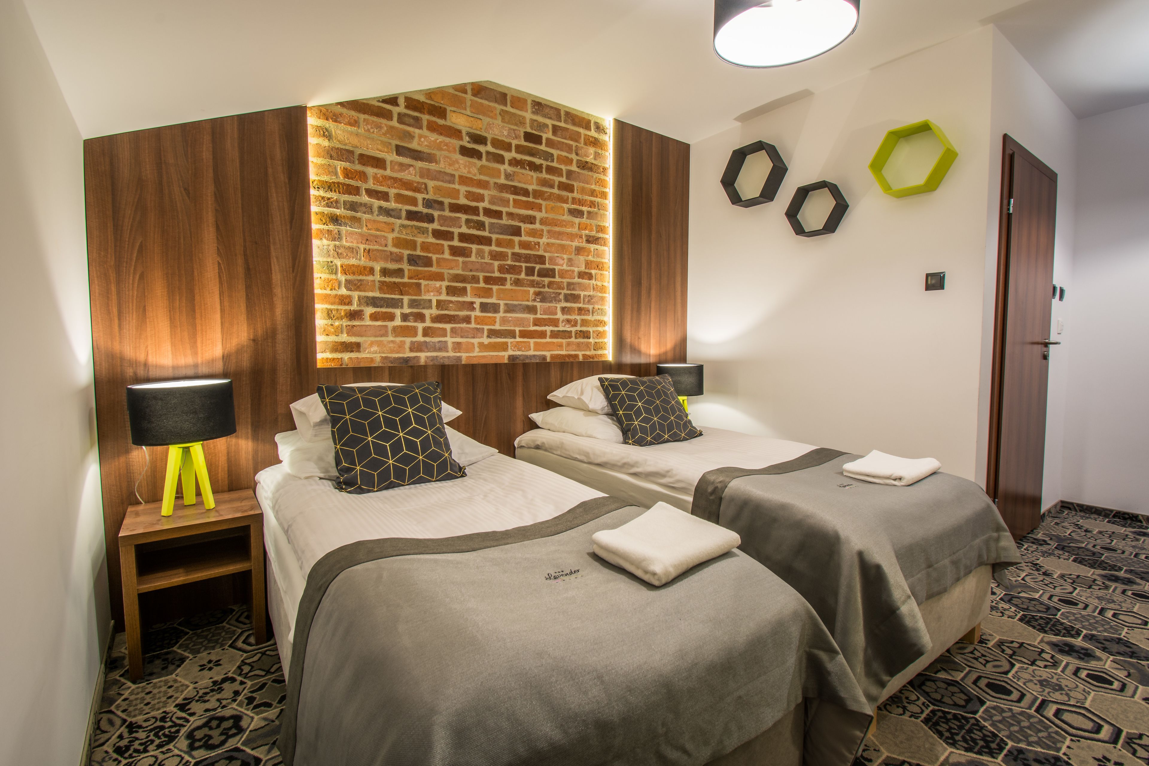 A hotel room with two beds, a brick accent wall, and a patterned floor.