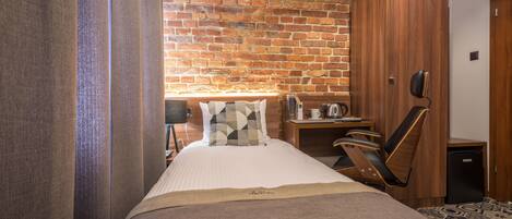 Una habitación de hotel con pared de ladrillo, cama con almohada estampada, escritorio con lámpara y armario.